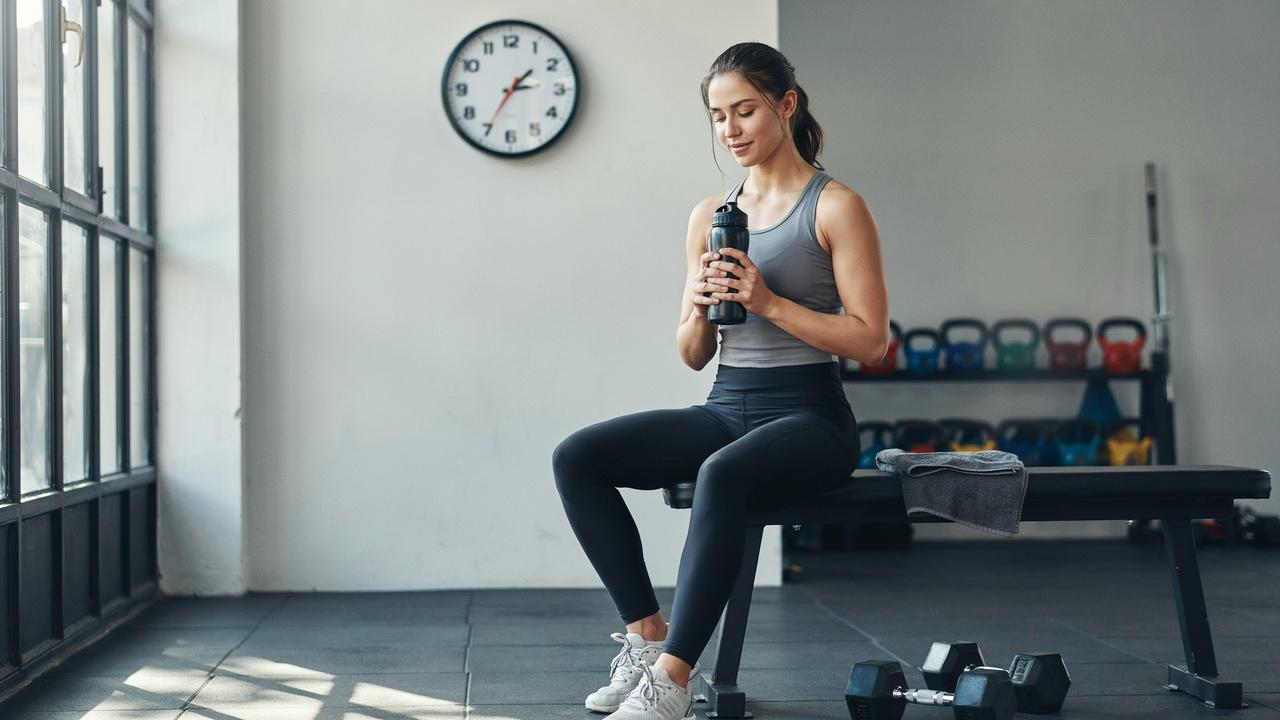 Person sitting on a gym bench, resting between sets, with dumbbells nearby.