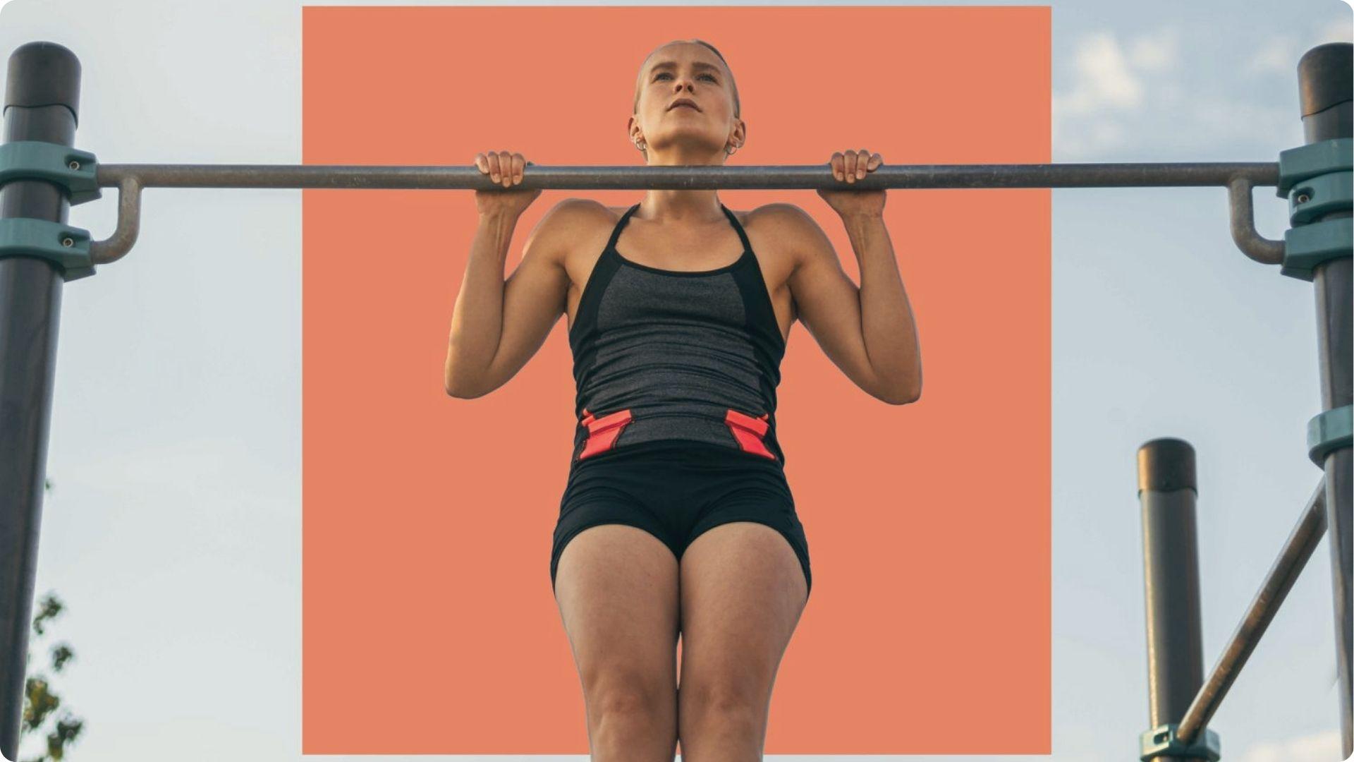 Woman in black tank doing pull-up with orange graphic backdrop, core and delts tight