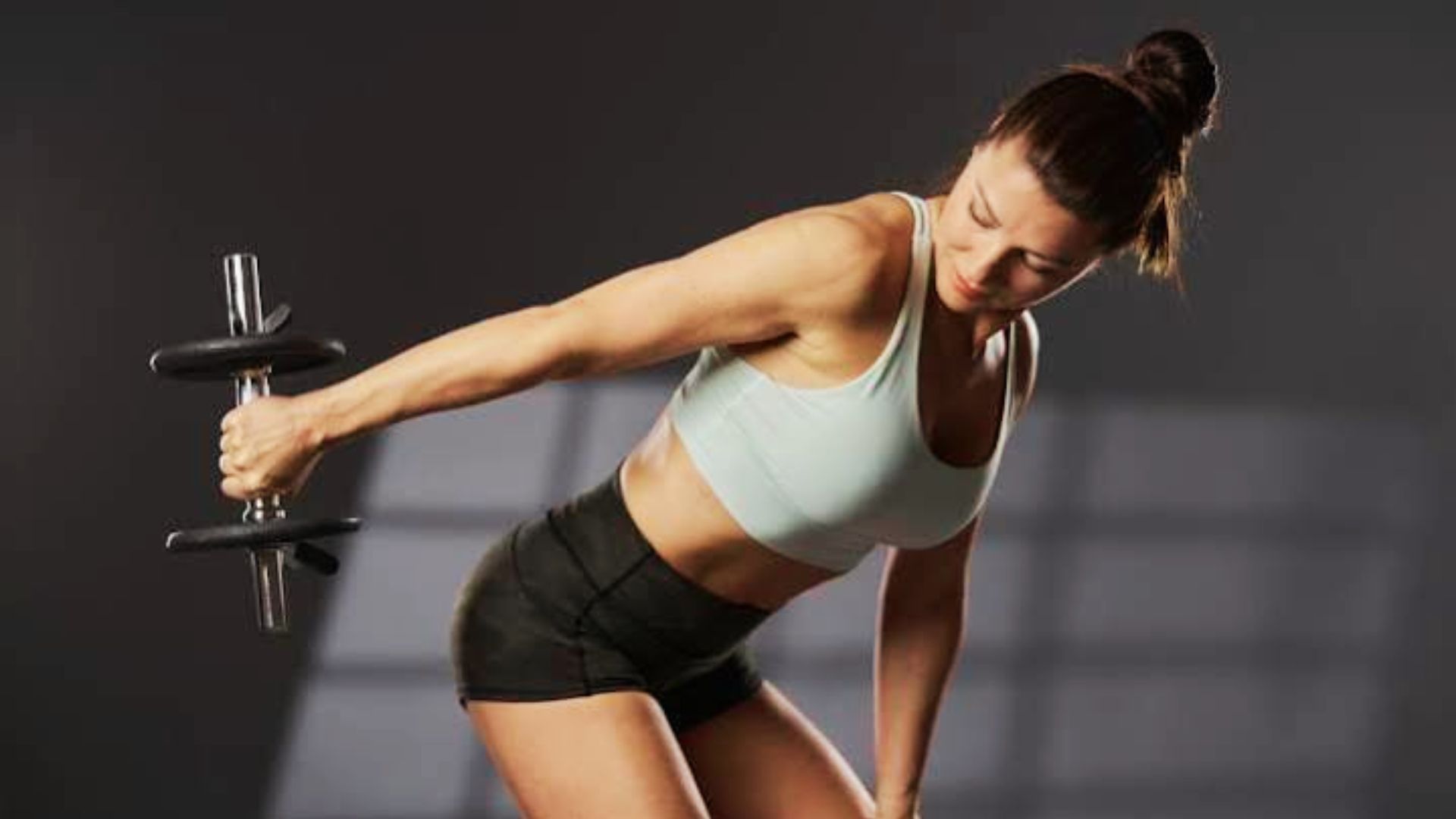 Woman performing bent-over dumbbell lateral raise in gym, engaging rear deltoids and triceps for upper body strength