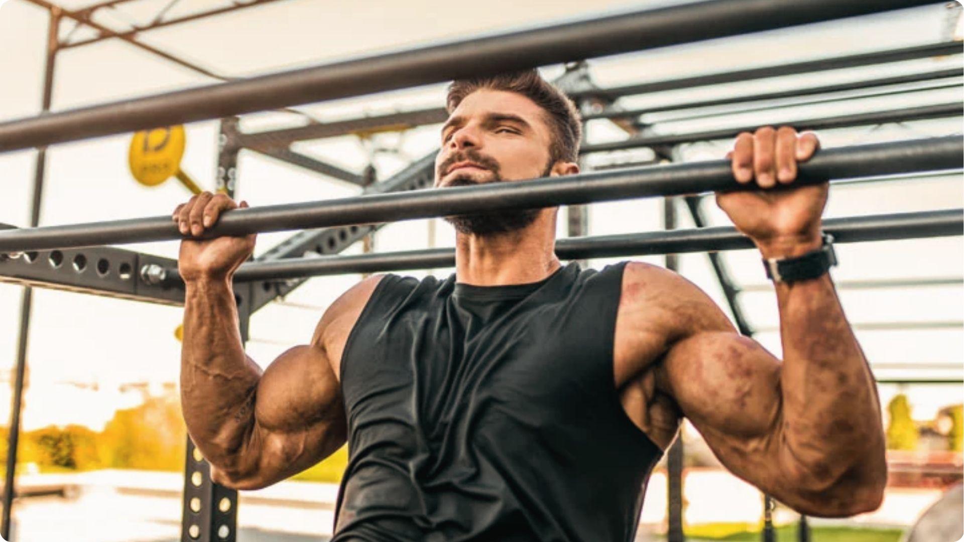 Bearded man in black tank doing outdoor pull-up, vascular arms and delts under tension