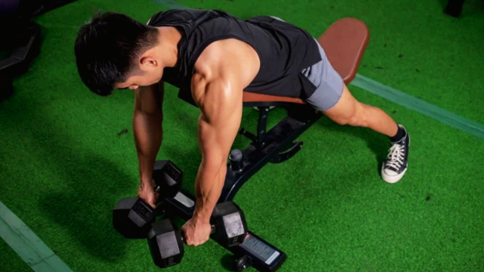 Man doing a bench bird dog row, lifting a dumbbell while balancing on one knee and opposite hand.