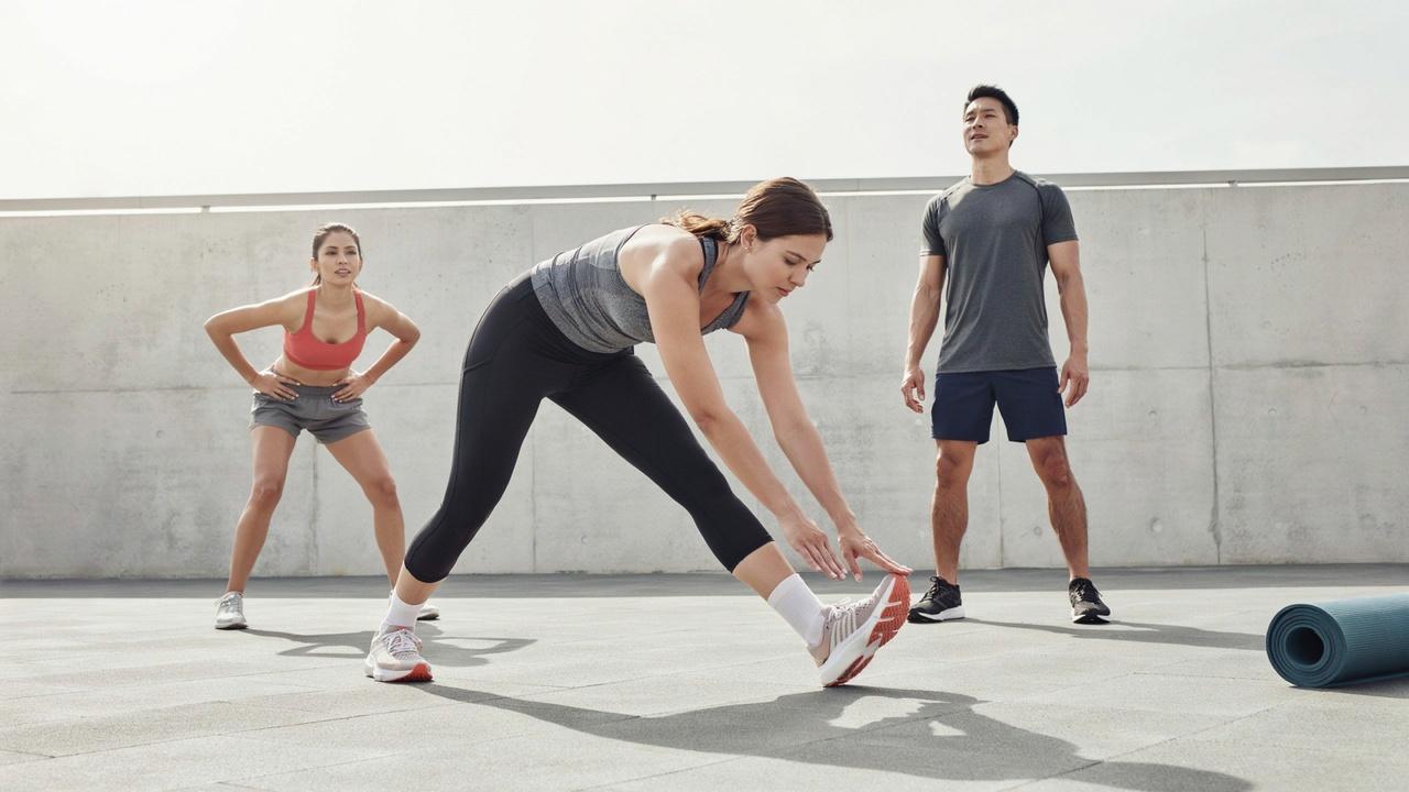 Three persons doing toe touches, shoulder rolls, and hip circles during a warm-up workout.