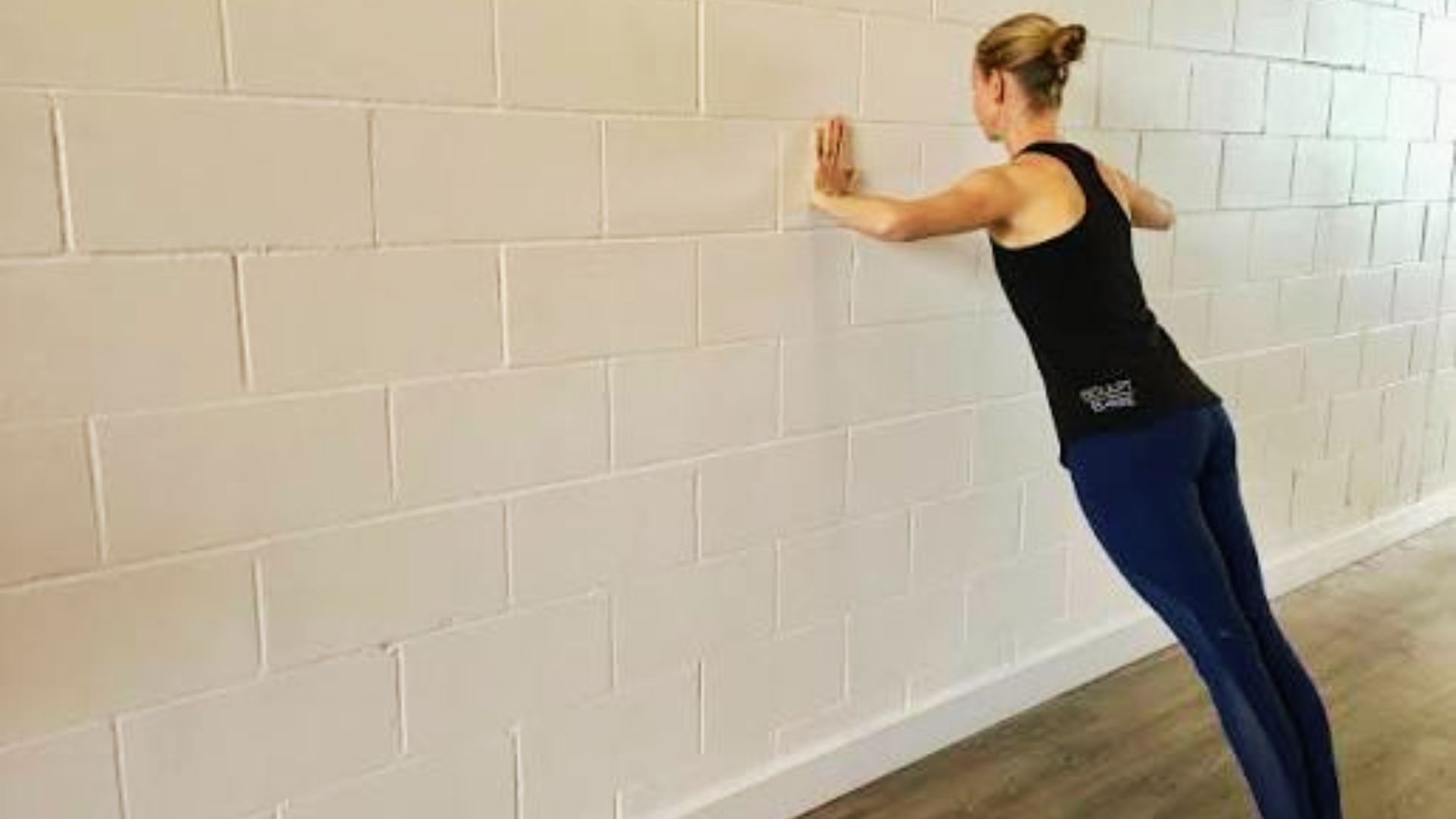 Woman demonstrating wall push-up form against white brick wall