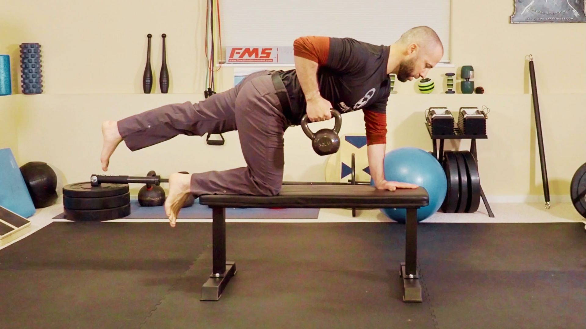 A side-view of a man on a weight bench performing a kettlebell bird dog row.