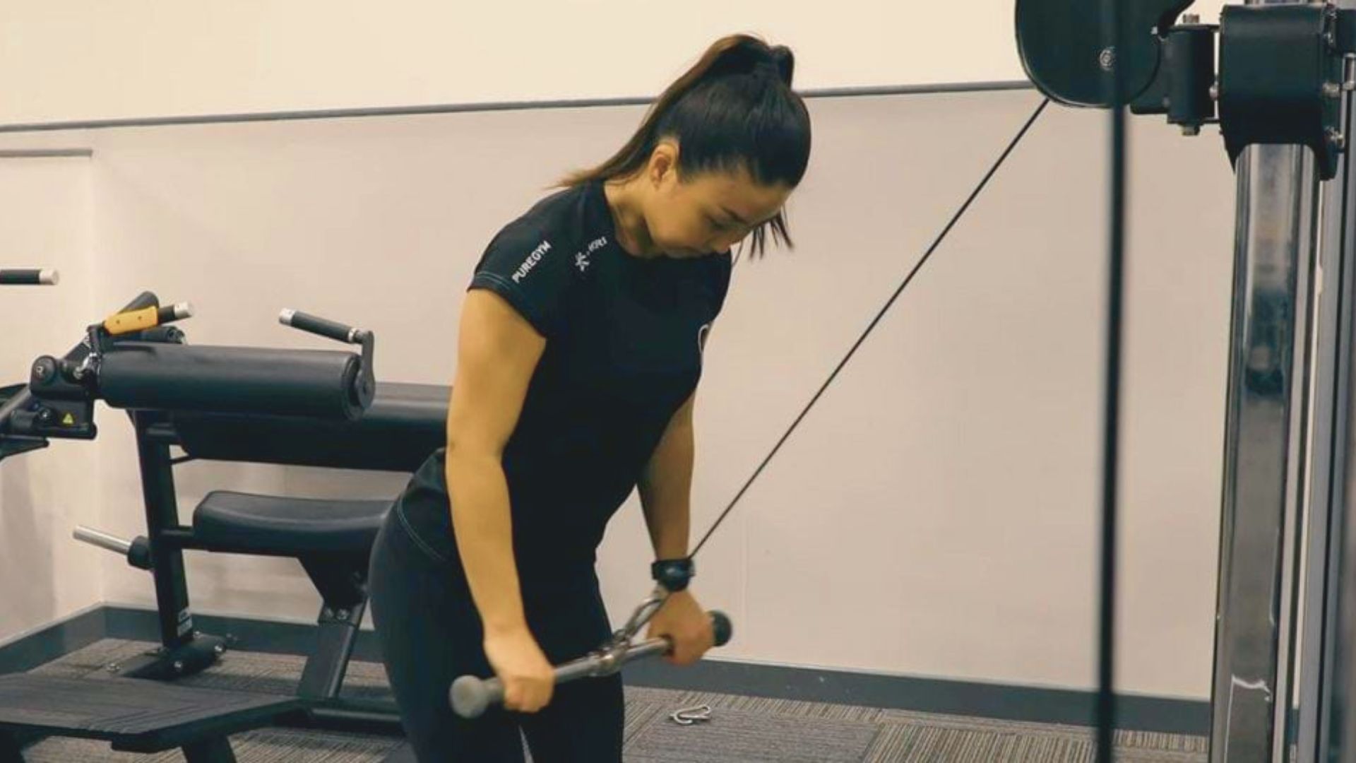 A woman performing a rope pushdown using a cable machine in a gym.