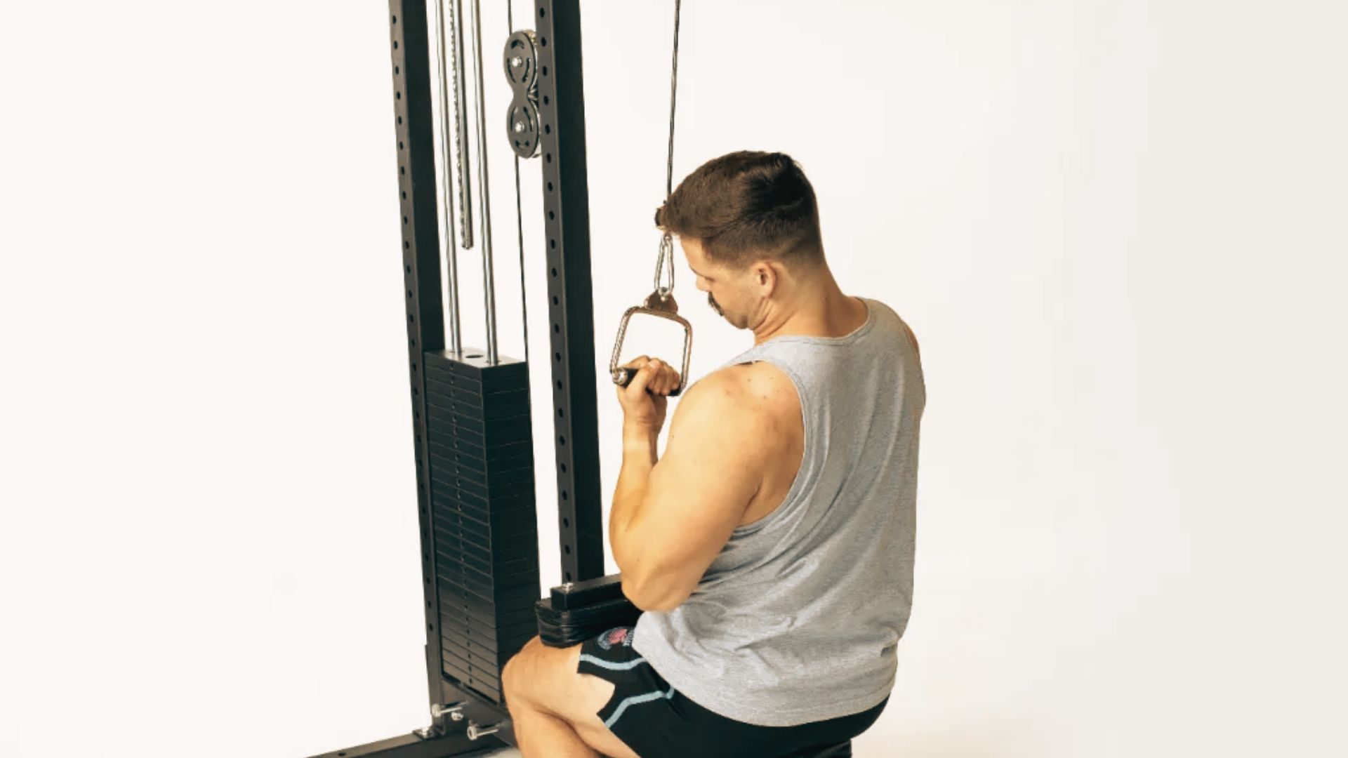 A man in a grey tank top performs a single-arm seated cable row with a D-handle attachment.
