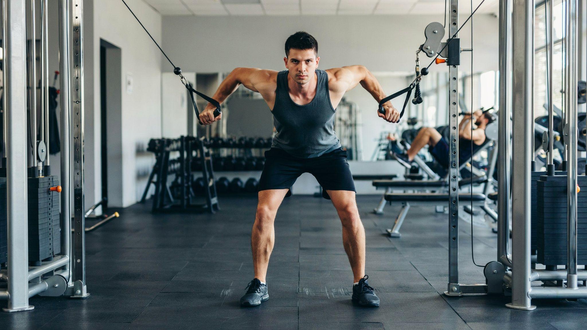 A man performing a standing cable fly exercise inside a gym.