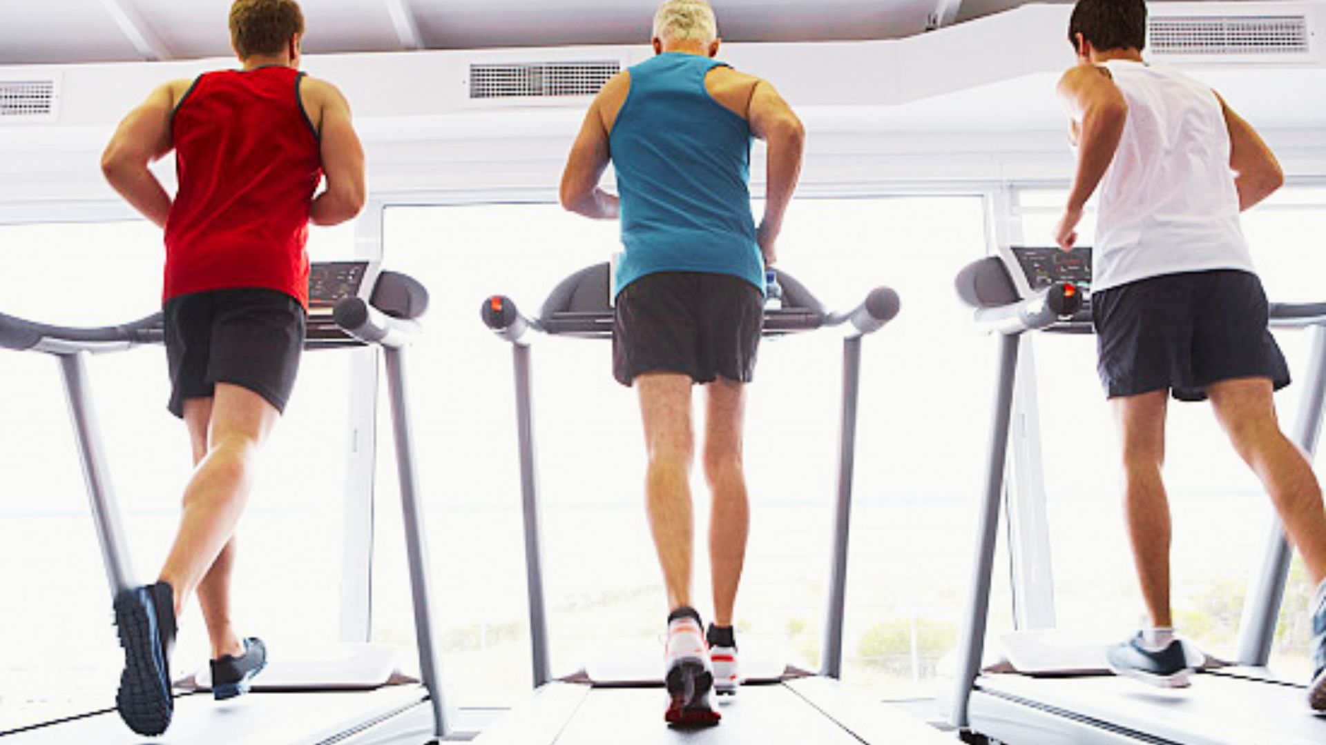 Three men in athletic wear run on treadmills side by side in a bright, modern gym.