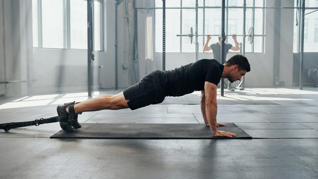 A male athlete in gym clothes holds the top of a Nordic curl, showing the isometric phase with tight muscles.