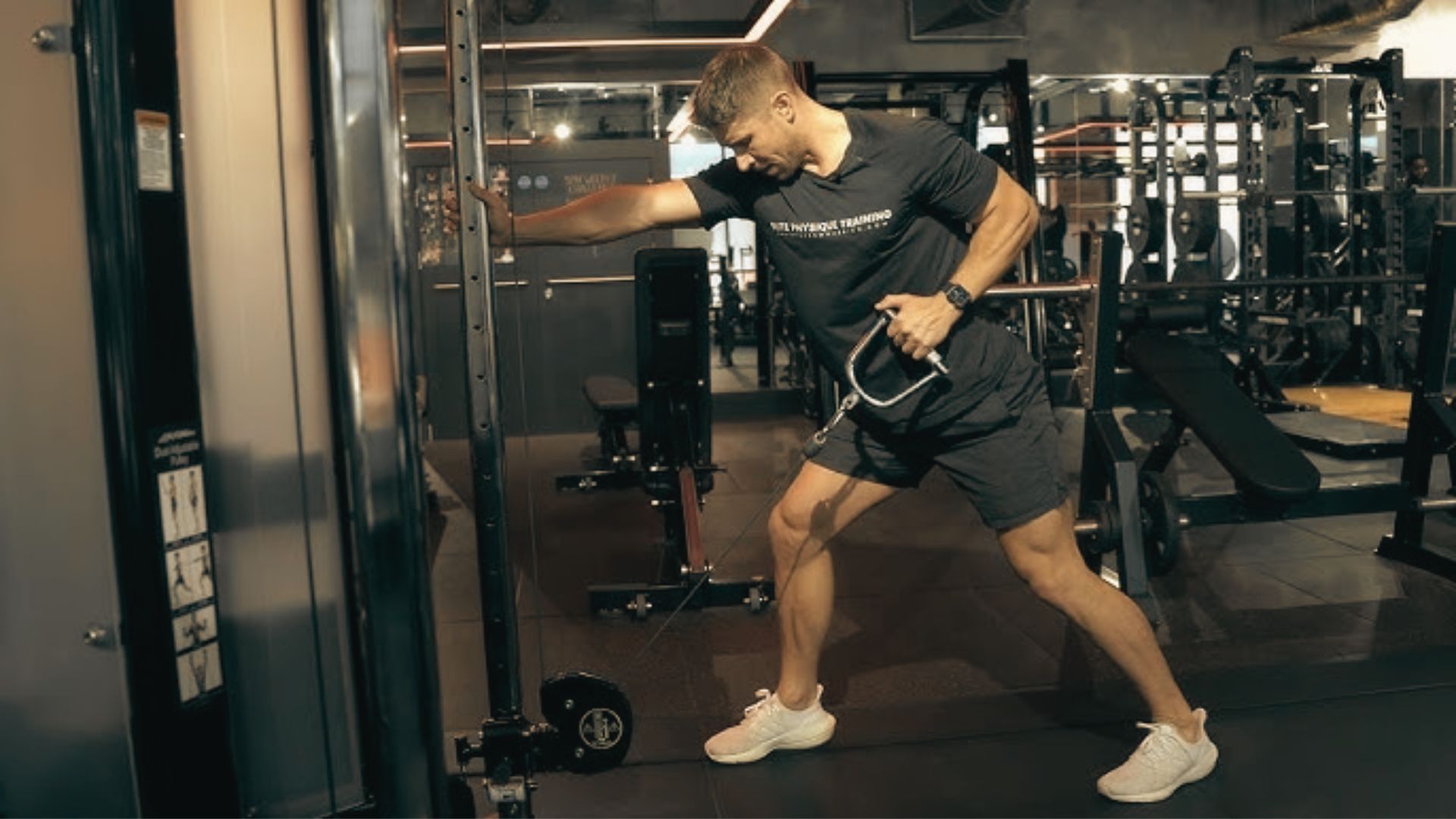 Athlete in a black tee and white shoes doing a single-arm low cable row while bracing against the machine.
