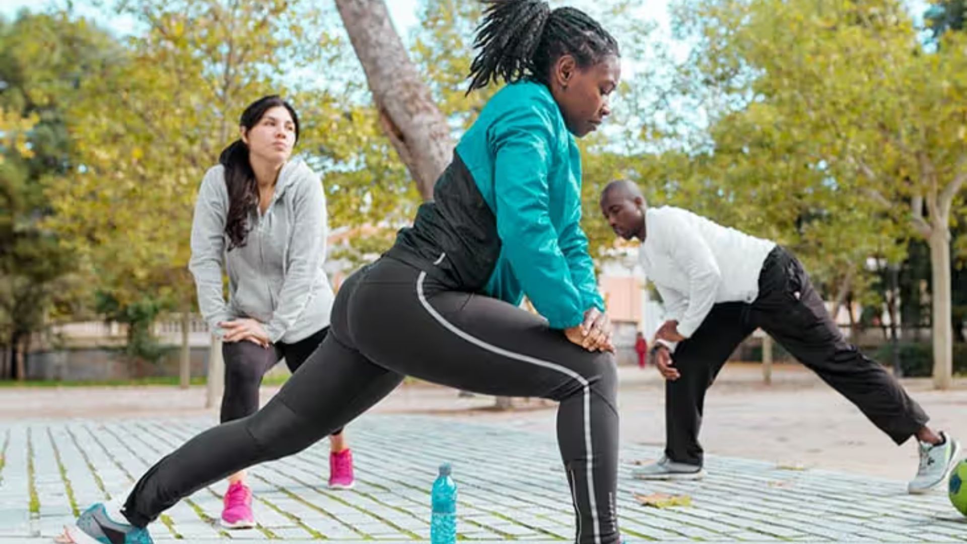 Group of three people doing side lunges in a park to warm up their lower body.