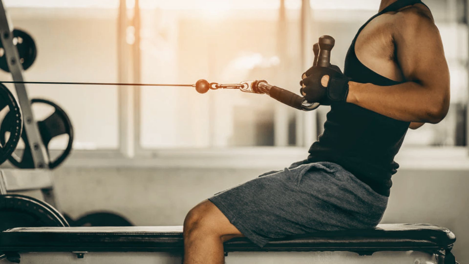 A man in a black tank top performs a seated cable row using a V-bar attachment in a gym.